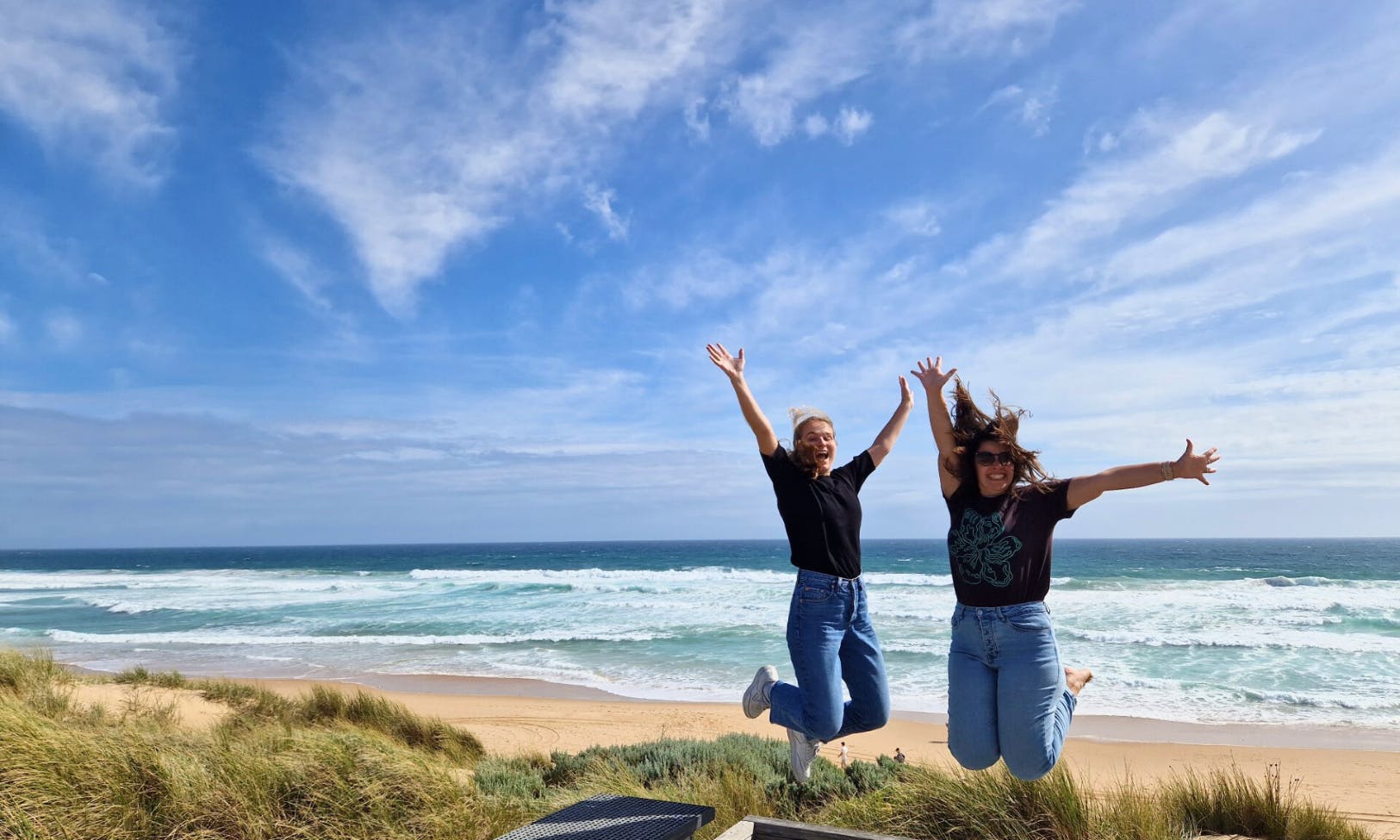 两个人愉快地在海滩上跳跃，海浪和蓝天，背景是分散的云彩。