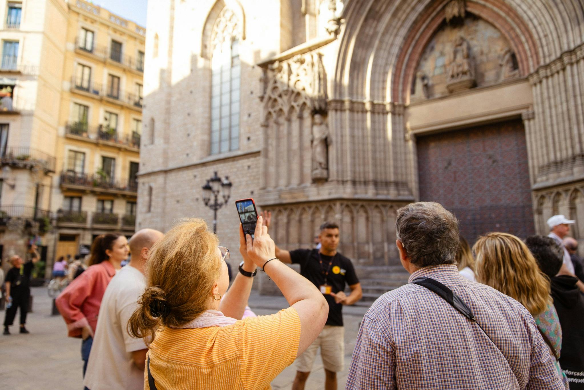 Un groupe de personnes écoutant un guide devant un bâtiment historique avec une entrée voûtée détaillée.