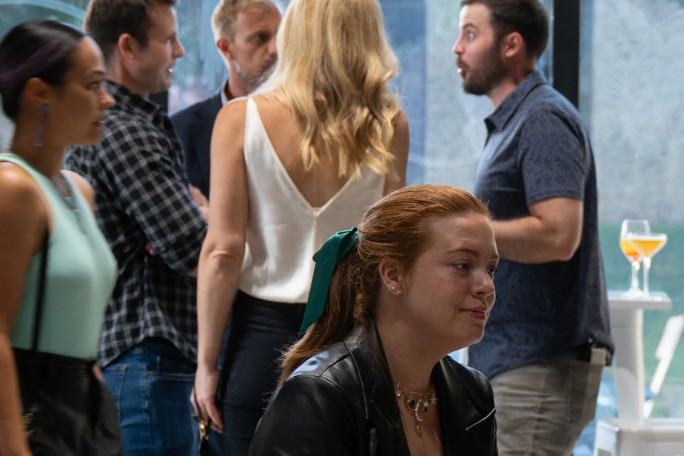 A group of people socializing in a modern indoor setting with large windows and white furniture.