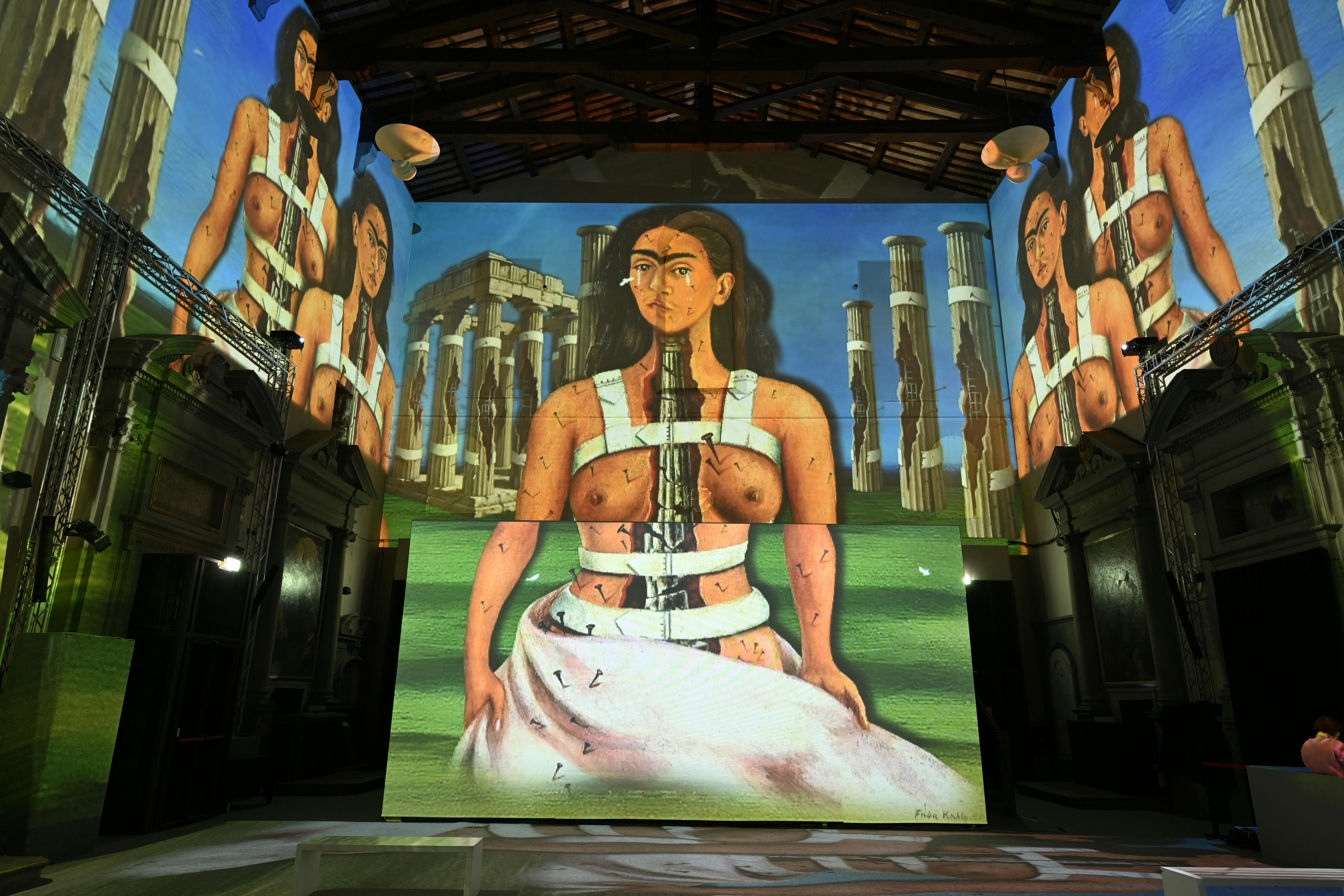 A projected artwork featuring a woman with a fractured body in a surreal setting with columns, displayed in a dark room.