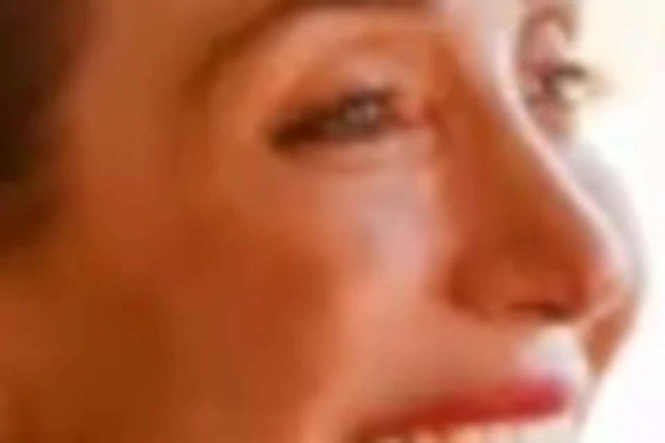A woman dressed casually is smiling while dining at a restaurant table with wine glasses and plates in front of her.