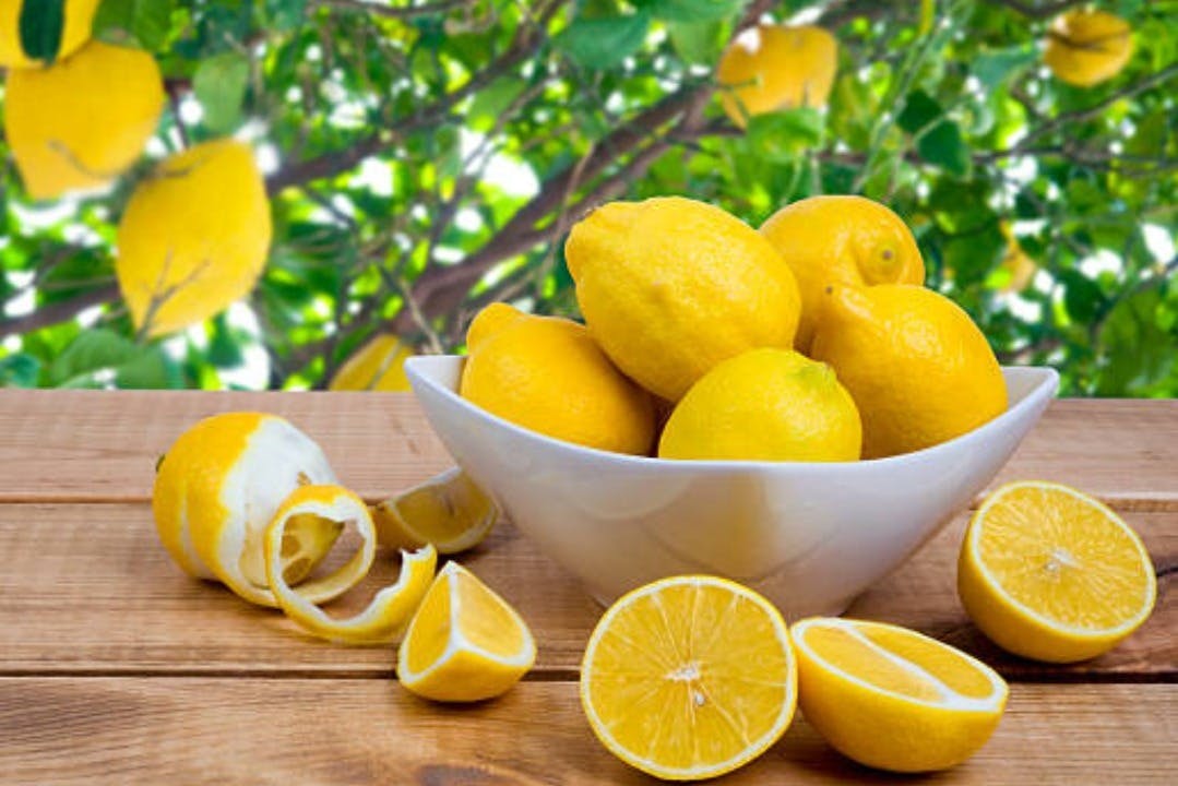 木製の表面にレモンを詰めた白いボウル。レモンの半分、スライス、皮が周りにあります。葉っぱのような背景。