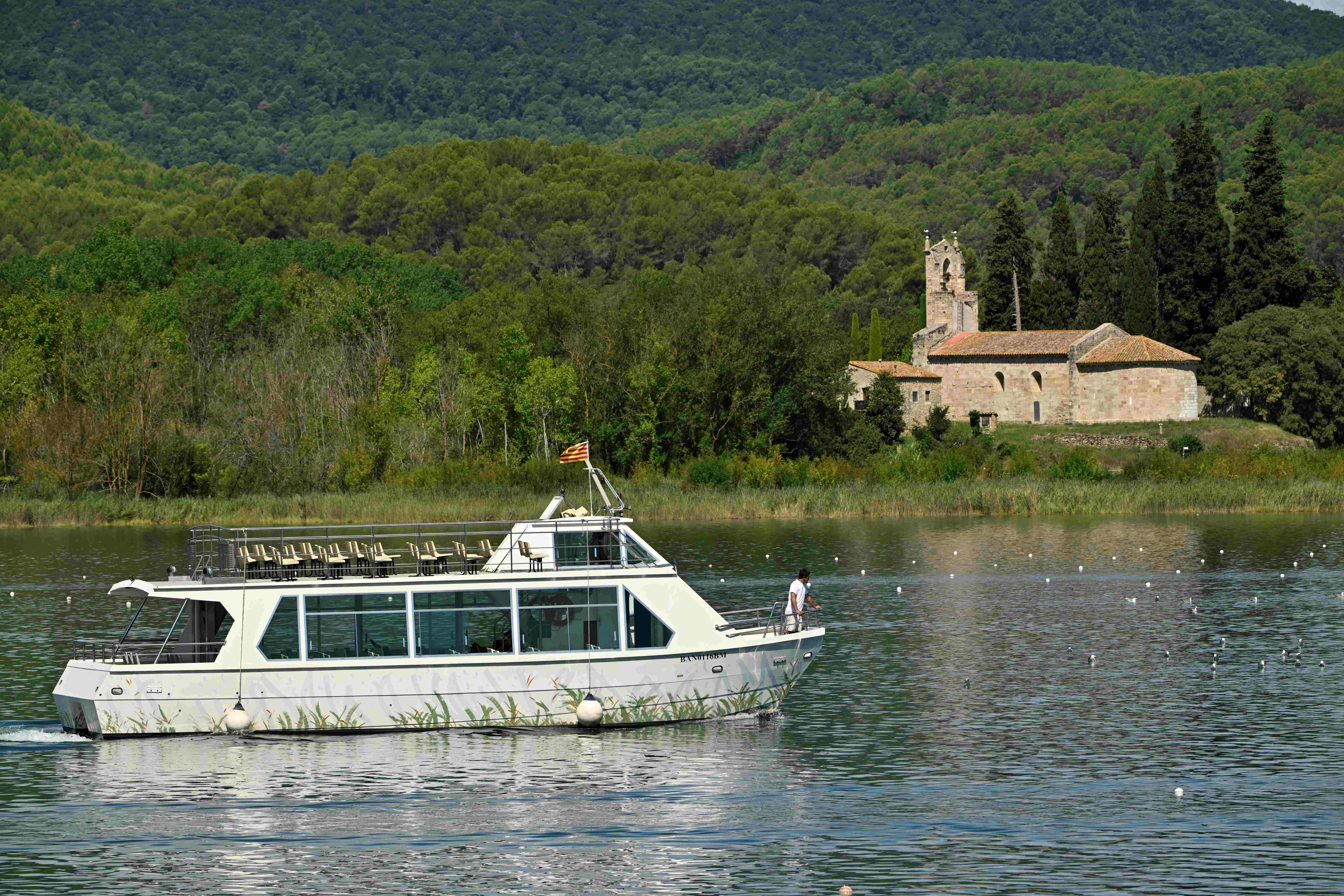 Una barca bianca su un lago con colline verdi sullo sfondo e una vecchia chiesa vicino alla riva.