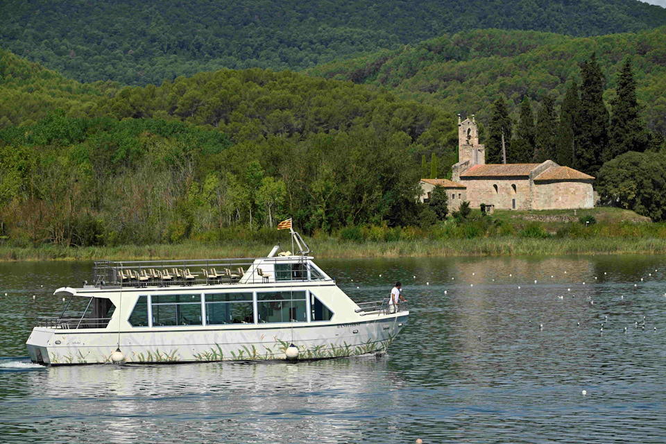 A white boat on a lake with lush green hills in the background and an old church near the shoreline.