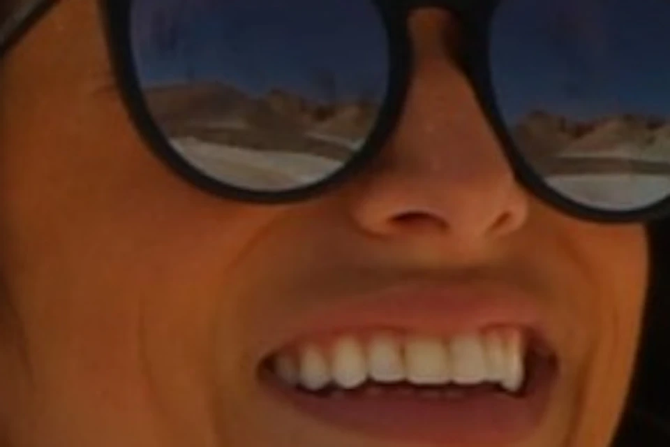 A woman in sunglasses and a hat smiles beside a directional sign for "KV.2 Ramesses IV" in a desert landscape with hills.