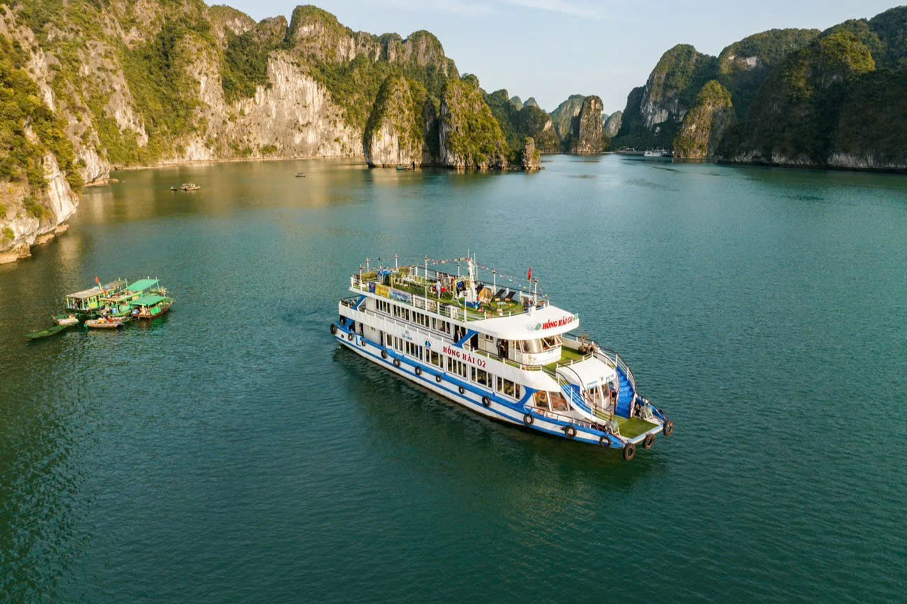 A tourist boat sails through a peaceful bay surrounded by tall, rocky islands under a clear sky.