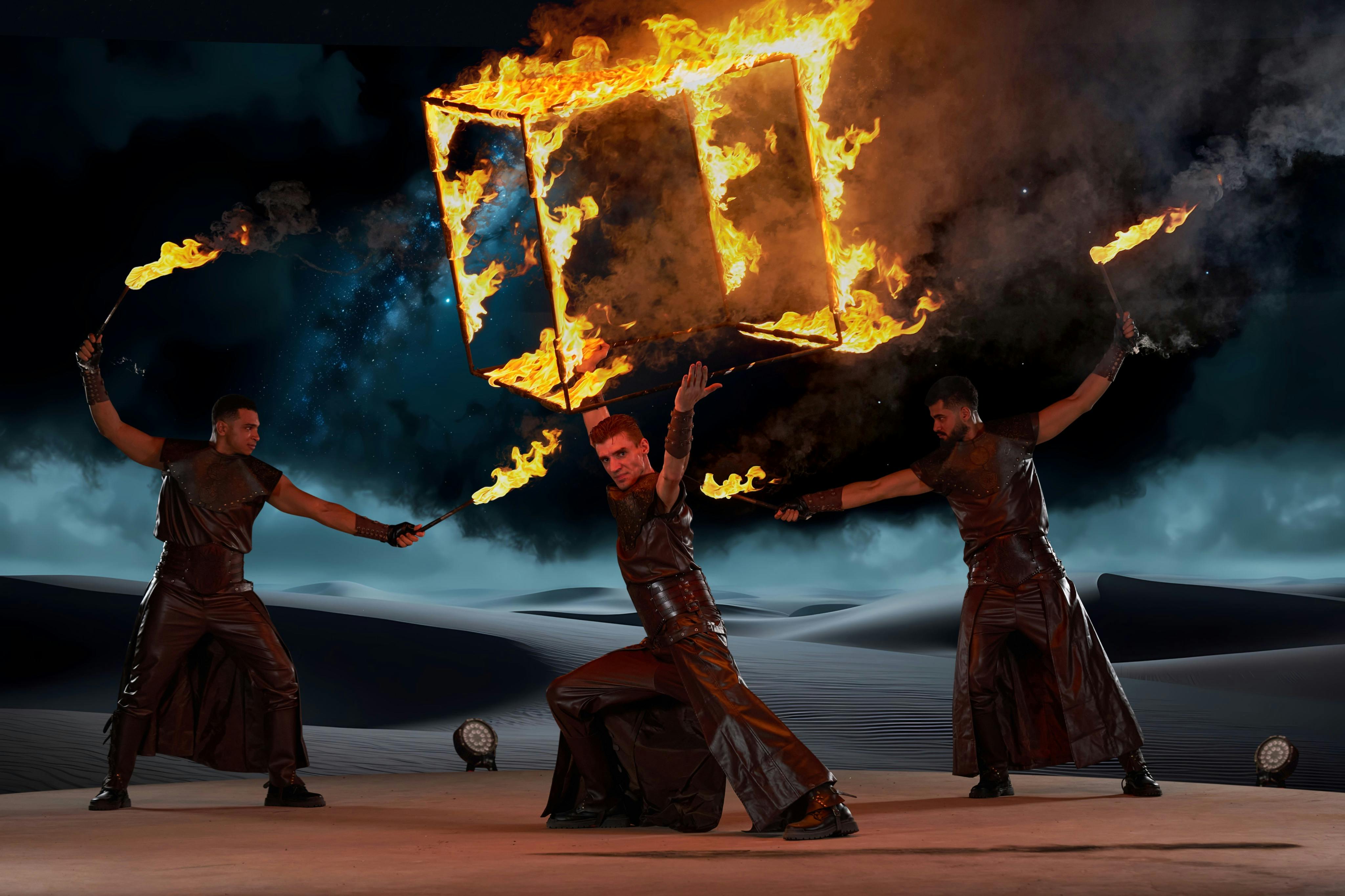 Twee performers in leren outfits manipuleren vlammende voorwerpen tegen een donkere achtergrond met sterren en zandduinen.