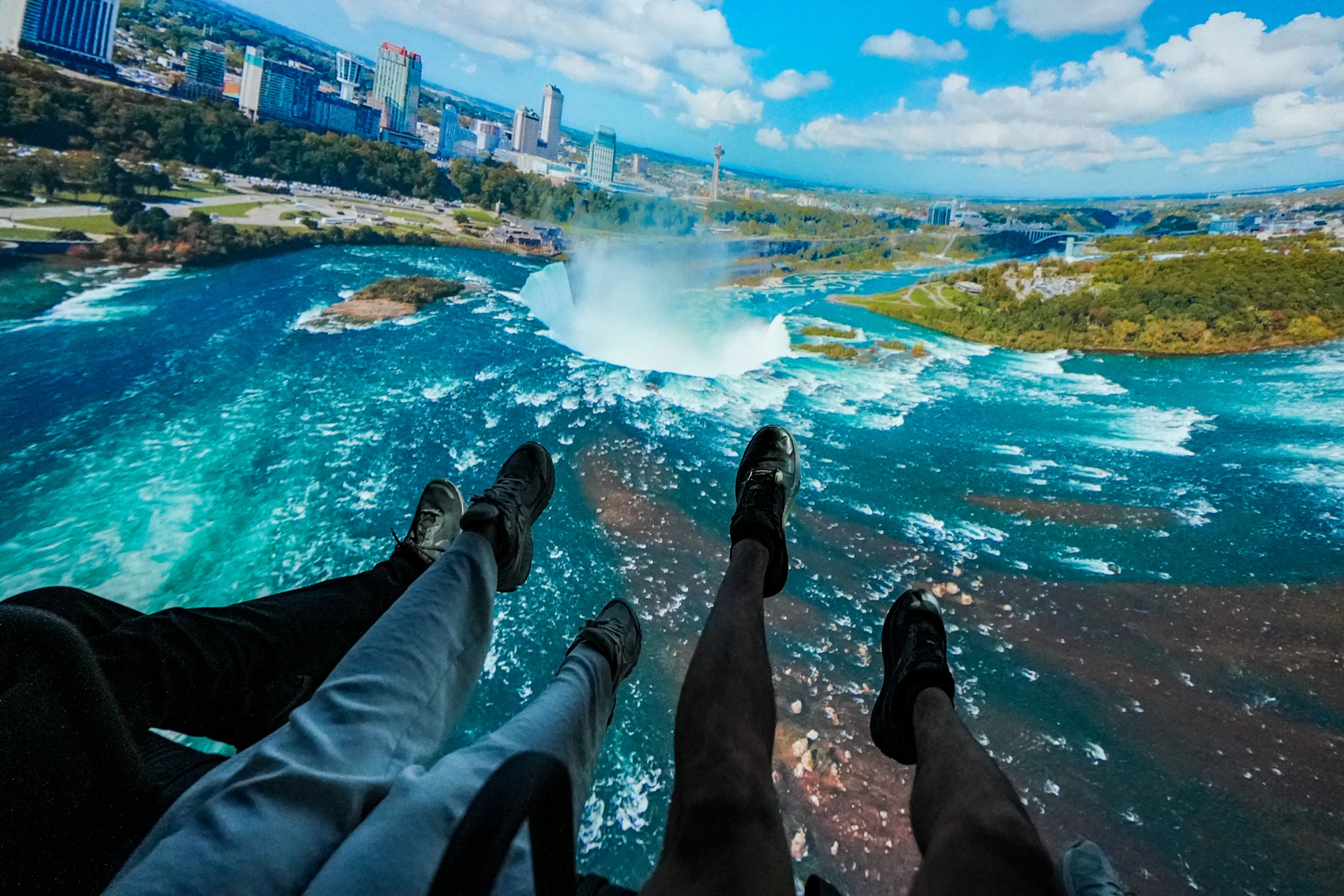 Four people suspended over a large waterfall with a cityscape visible in the background.