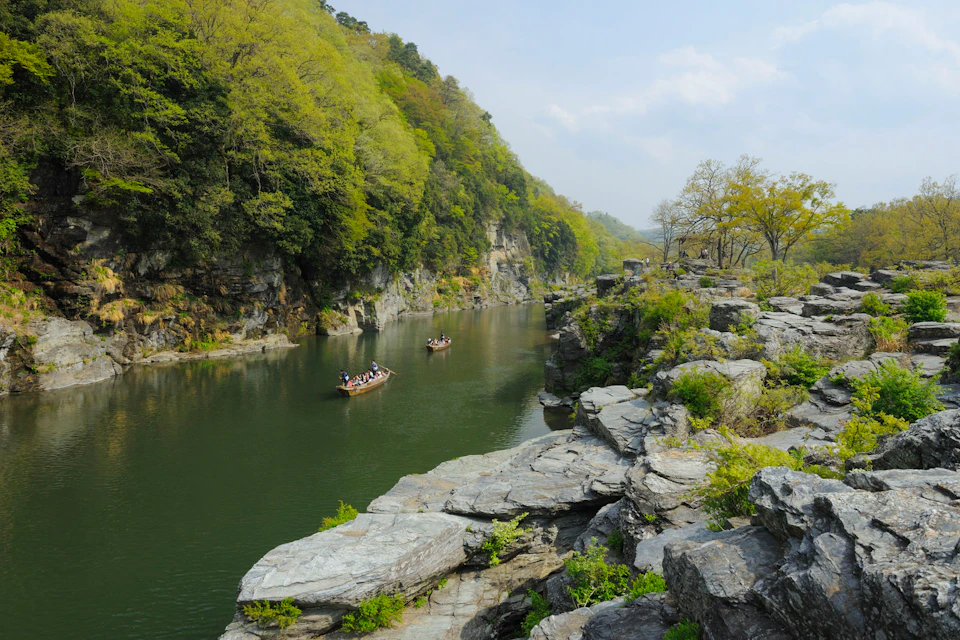 A scenic river surrounded by rocky cliffs and lush green trees, with people in rowboats enjoying the calm water.