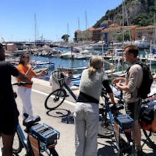 Fyra personer med cyklar står vid en småbåtshamn med dockade båtar och pratar en solig dag.