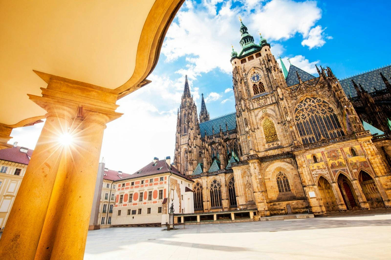 Sunny courtyard view of St. Vitus Cathedral, featuring Gothic architecture with pointed spires and detailed stonework.