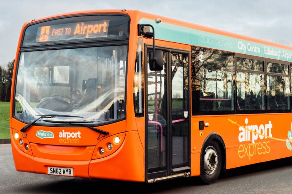 Orange flygbuss med "Snabbt till flygplatsen". Det har gröna accenter och är märkt "Bright Bus" med registreringsskylten SN62 AYB.