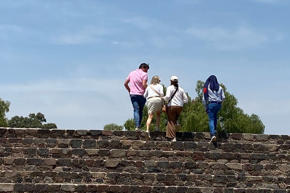 Four people walking up a stone staircase with trees and a clear sky in the background.