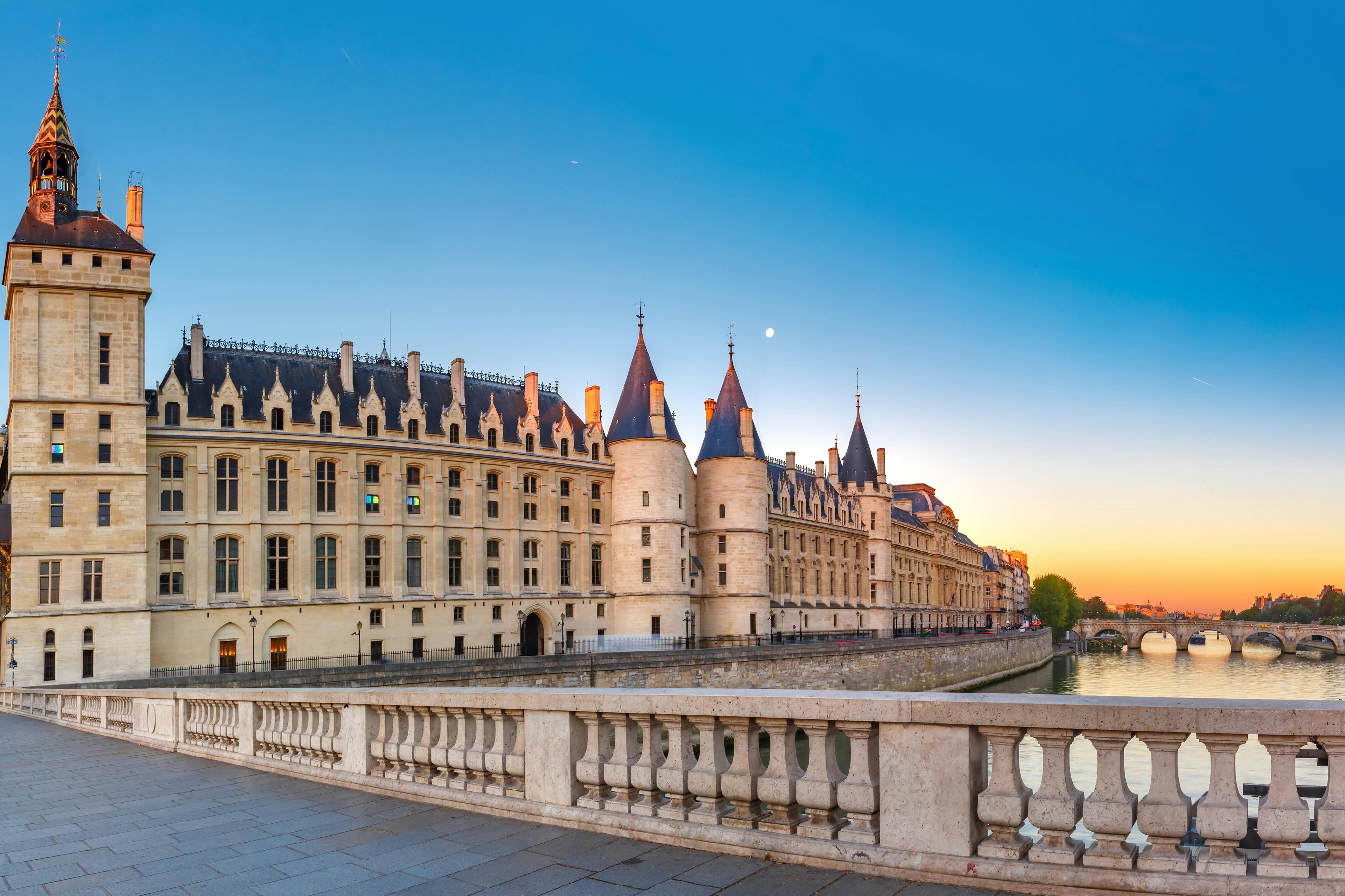 A historic building with towers along a river at sunset, viewed from a stone bridge.