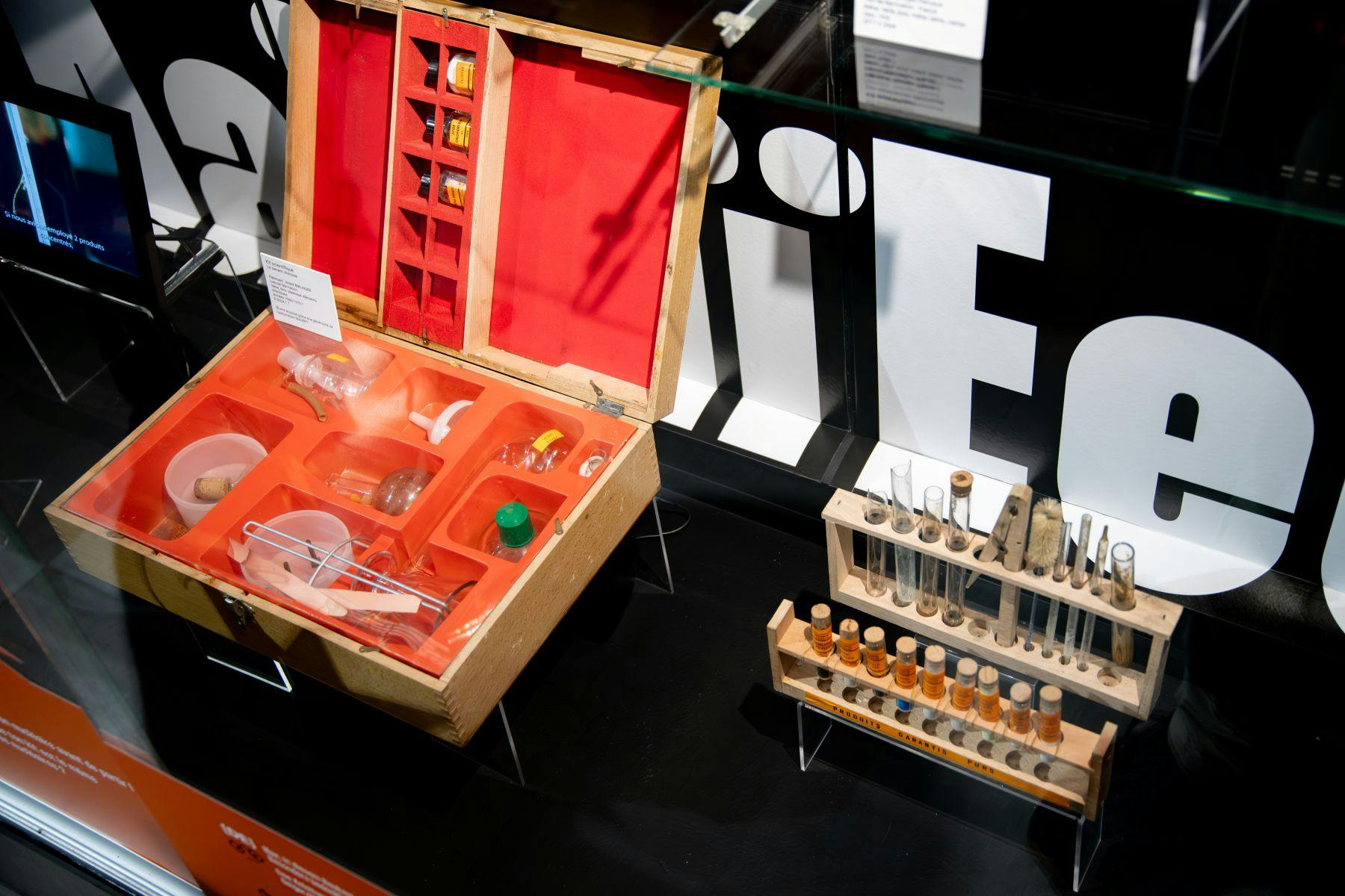 テストチューブ、ビーカー、ボトルを含むビンテージケミストリーセット付きのケースを、「LIFE」というテキストを背景にディスプレイします。