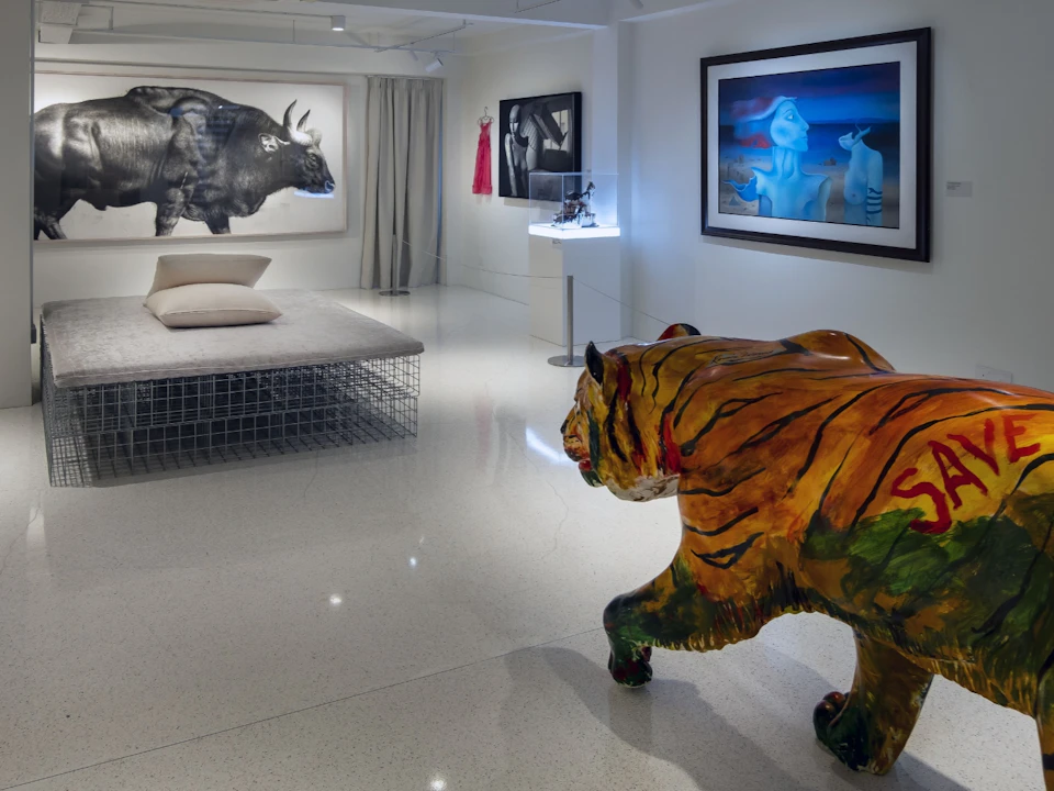 A modern gallery space with art pieces, including a large painted tiger sculpture, and various artworks displayed on walls.