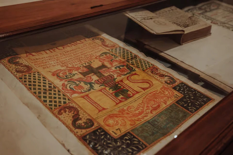 An ornate manuscript displayed under a glass case, featuring intricate patterns, text, and colorful religious imagery.