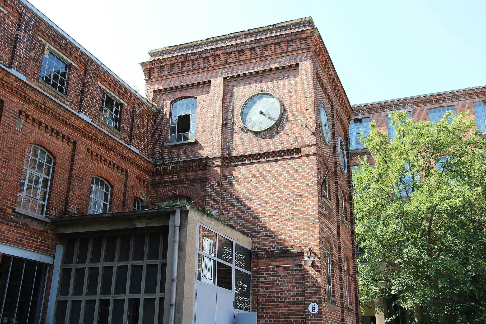 一栋红砖建筑，配有大窗户和钟楼。 右边有一棵树。