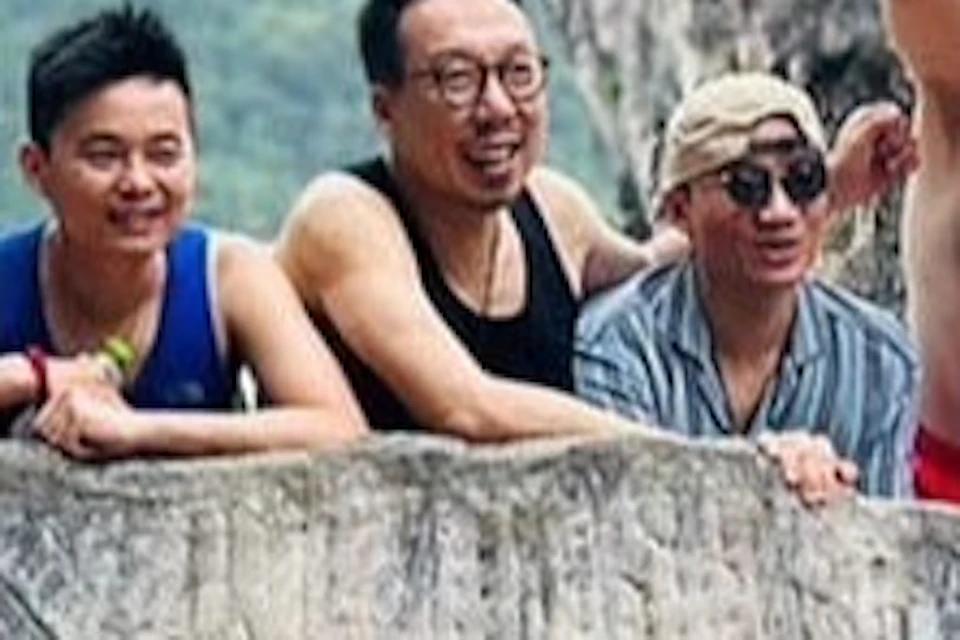 A group of people poses around a multilingual sign for James Bond Island with large rock formations and greenery in the background.