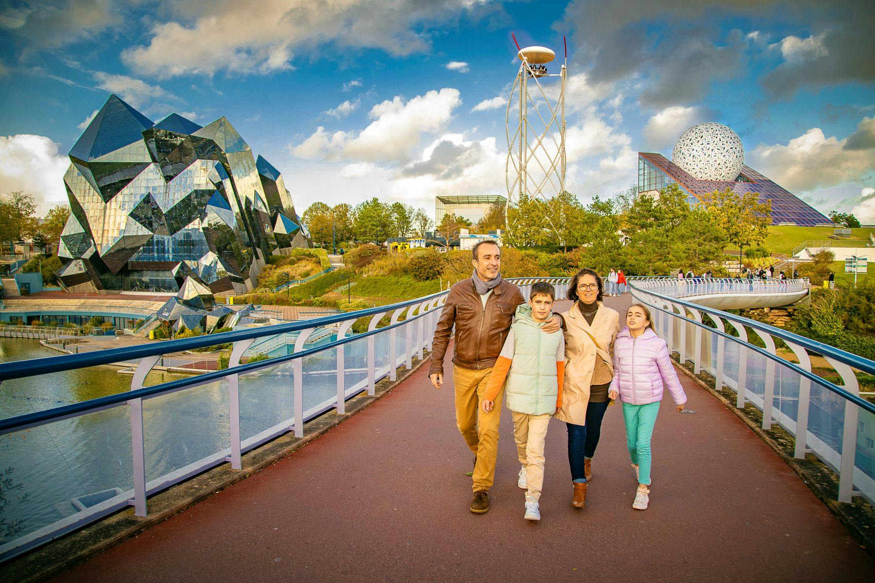 A family of four walking on a wide path with a futuristic park featuring dome and tower structures in the background.
