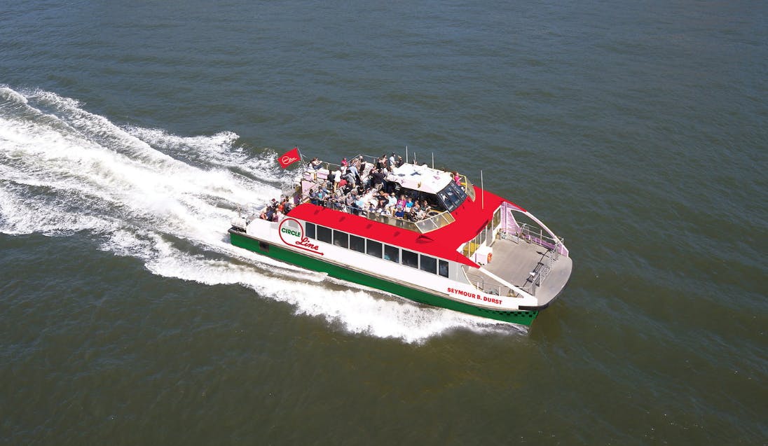 Loď jménem „Seymour B. Durst“ s červeno-bílou horní palubou, plnou cestujících, plující na otevřené vodě.