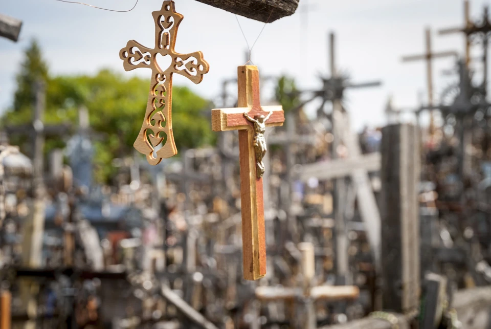 Two wooden crosses hanging in the foreground with many other crosses blurred in the background.