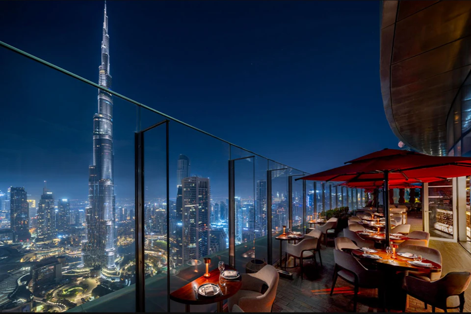 A rooftop restaurant at night with a view of an illuminated city skyline and the Burj Khalifa.