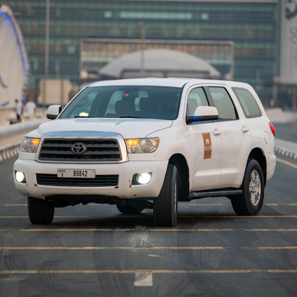 A white Toyota SUV with license plate "89842" driving on a city road with buildings visible in the background.