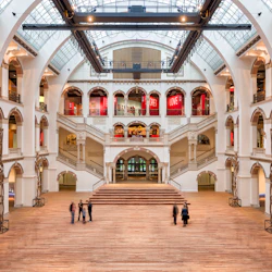 Rymlig hall i flera plan med välvda balkonger, trappor och flera besökare på ett trägolv. Röda banderoller med texten "LOVE" och "SECRET".