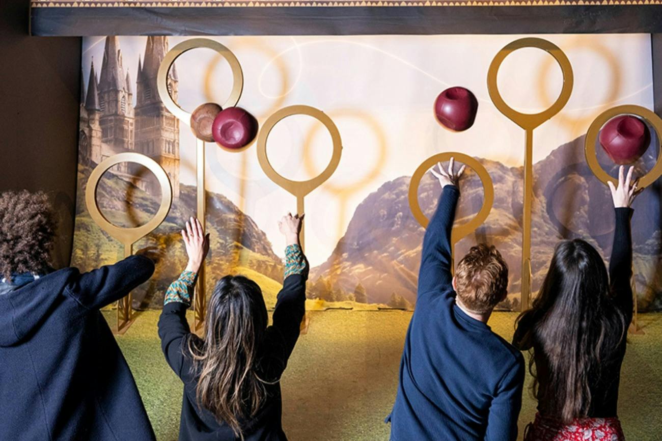 A group of people standing in front of a backdrop with hoops, throwing balls, resembling a Quidditch-themed activity.