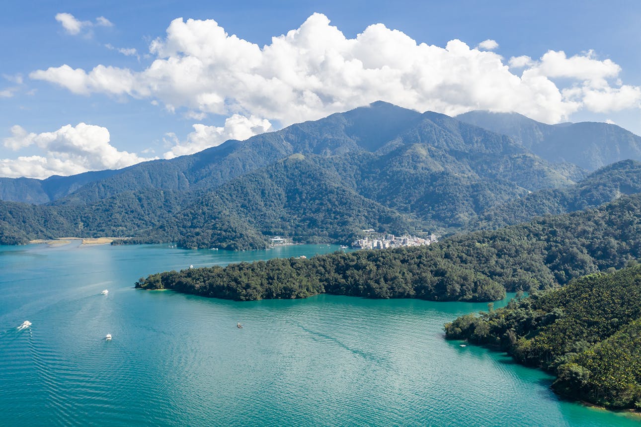 A serene lake surrounded by forested islands and mountains under a blue sky with scattered clouds.