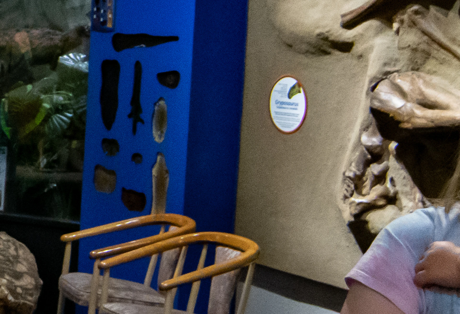 A large dinosaur exhibit with open mouth, three children observing and reacting in amazement, one child being held by an older girl.