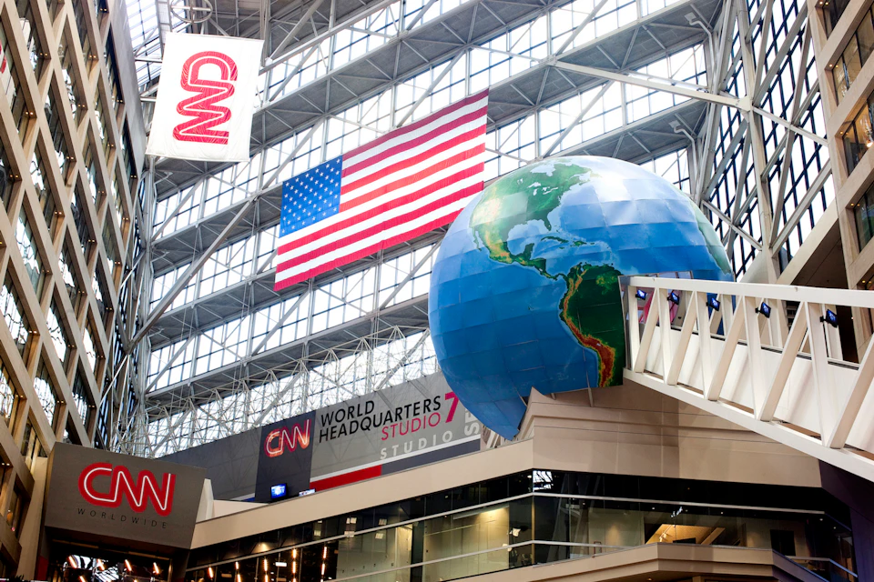 Interior view of CNN's headquarters with a large American flag, a globe sculpture, and multiple CNN logos.