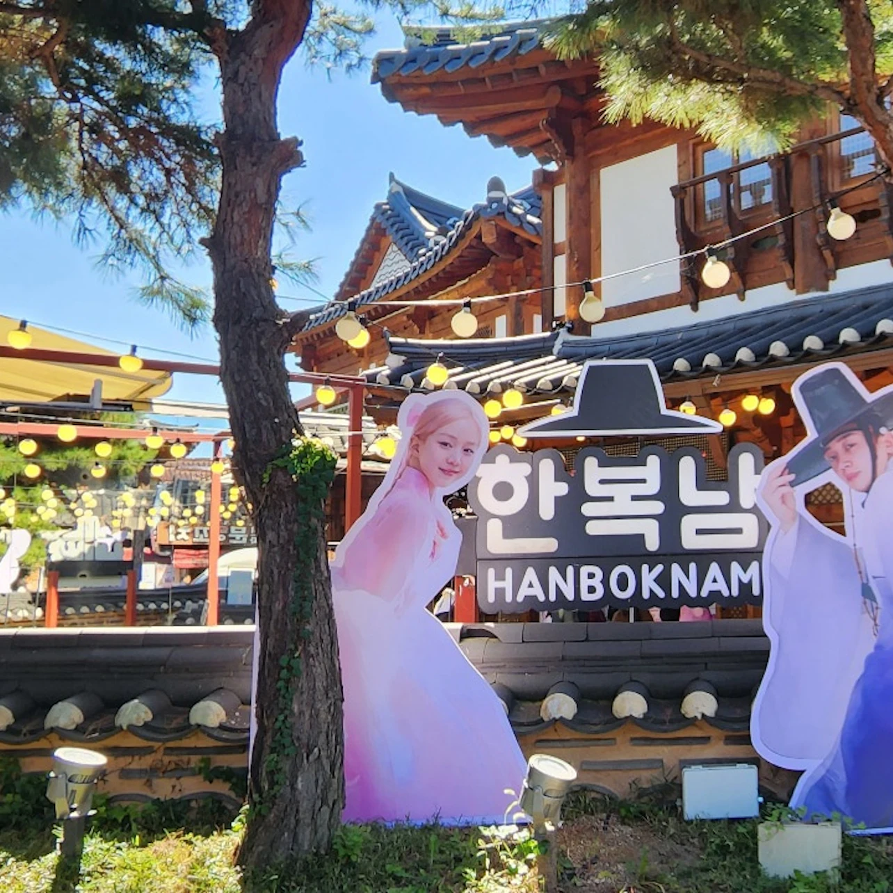 A traditional Korean building with cutouts of people in traditional attire and a sign reading 'Hanboknam' in front.