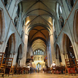 Insidan av en medeltida katedral med högt välvt tak, välvda pelare, trästolar och människor som sitter och går.