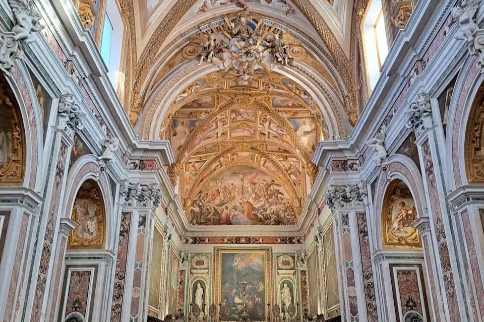 Elaborately decorated church interior with ornate frescoed ceiling, arched details, and richly adorned walls.