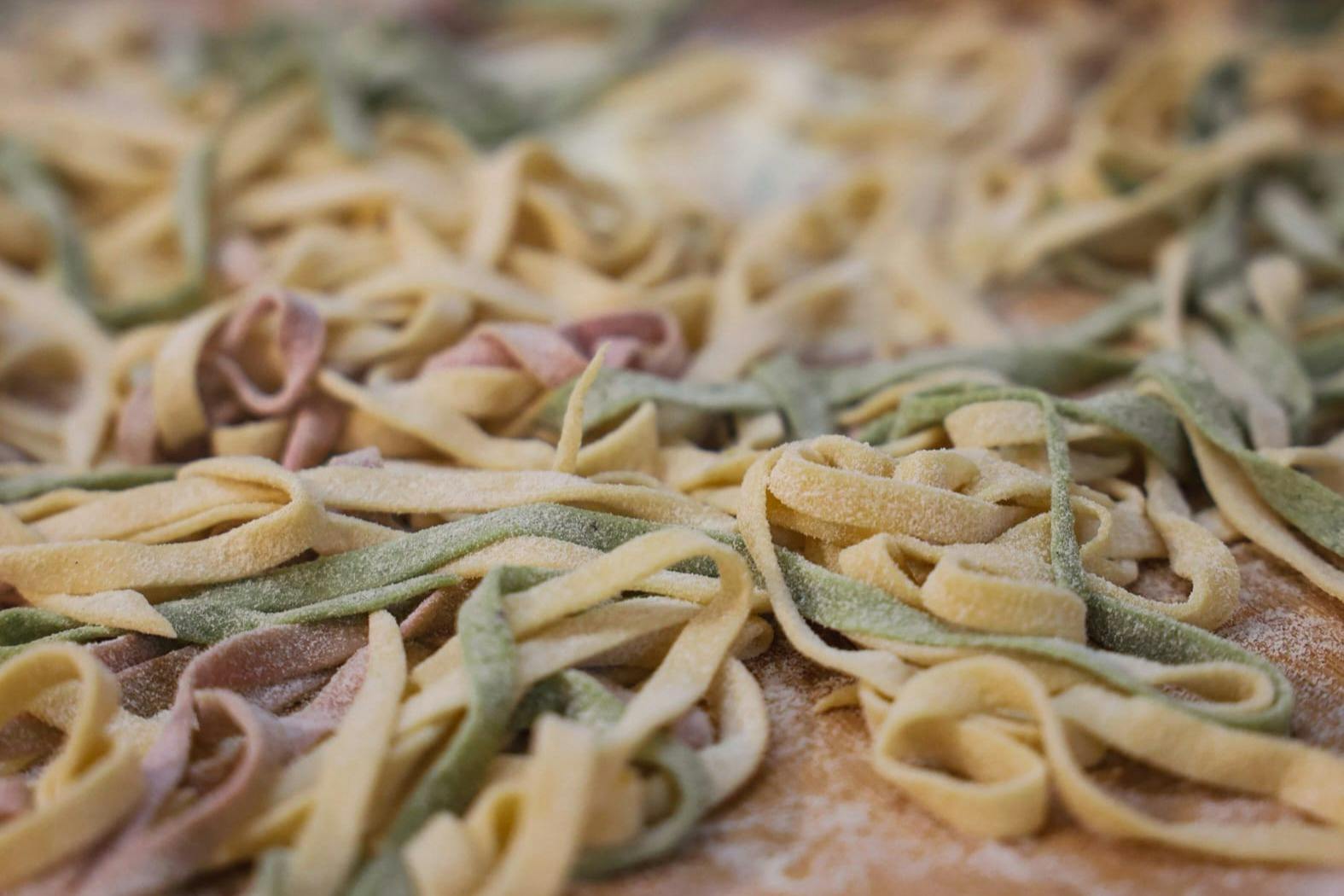 Primer pla de pasta fettuccine cruda en tres colors diferents (groc, verd i rosa) estesa sobre una superfície.