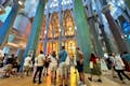 Interiøret i Sagrada Familia viser besøgende, der beundrer de imponerende søjler og farverige glasmosaikvinduer.