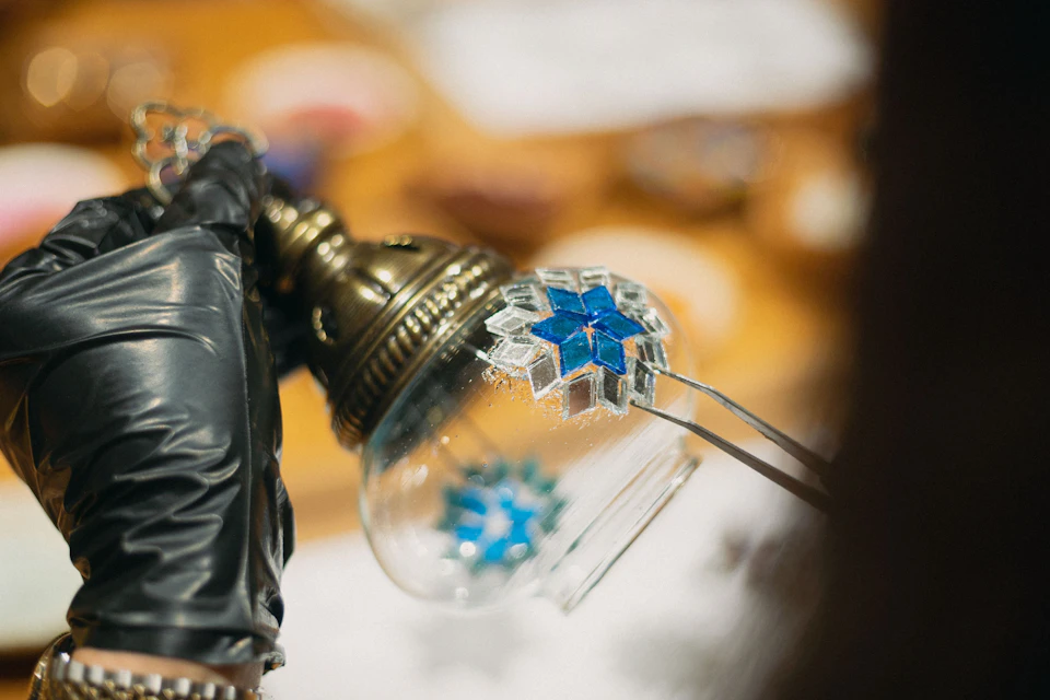 Close-up of a person in black gloves placing a blue mosaic piece on a glass sphere.