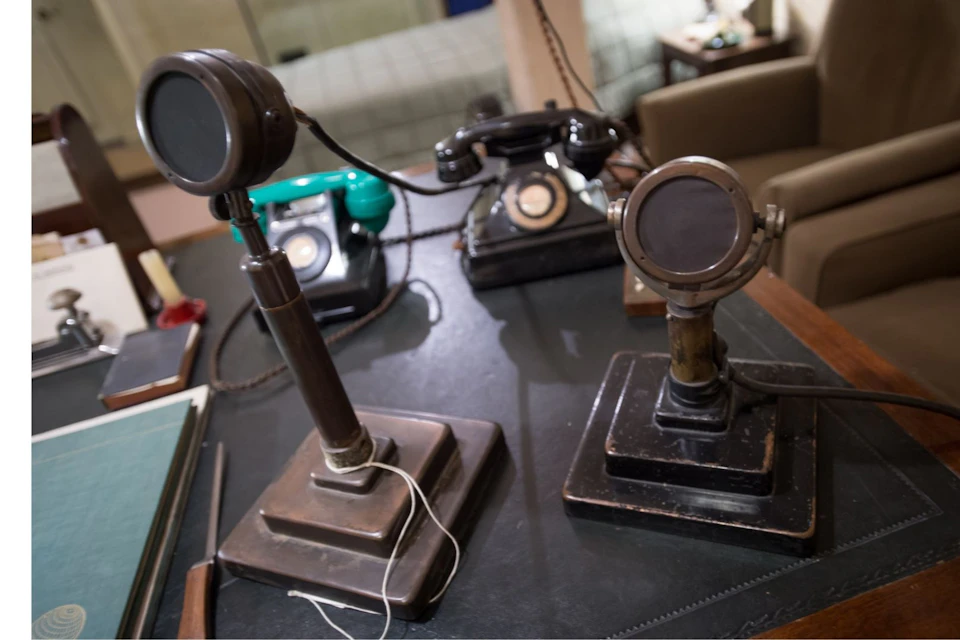 Two vintage microphones and telephones are on a desk in a retro office setting.