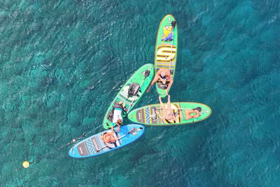 Four people relaxing on paddleboards clustered together on clear turquoise water.