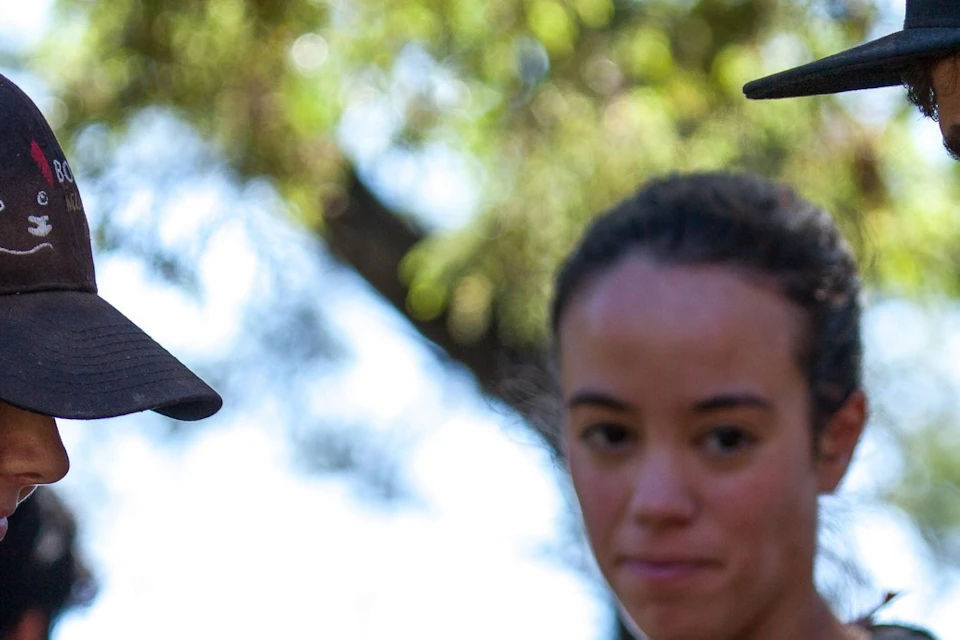 Three people are outdoors; one holds a wombat while another gently touches it. A third person watches attentively.