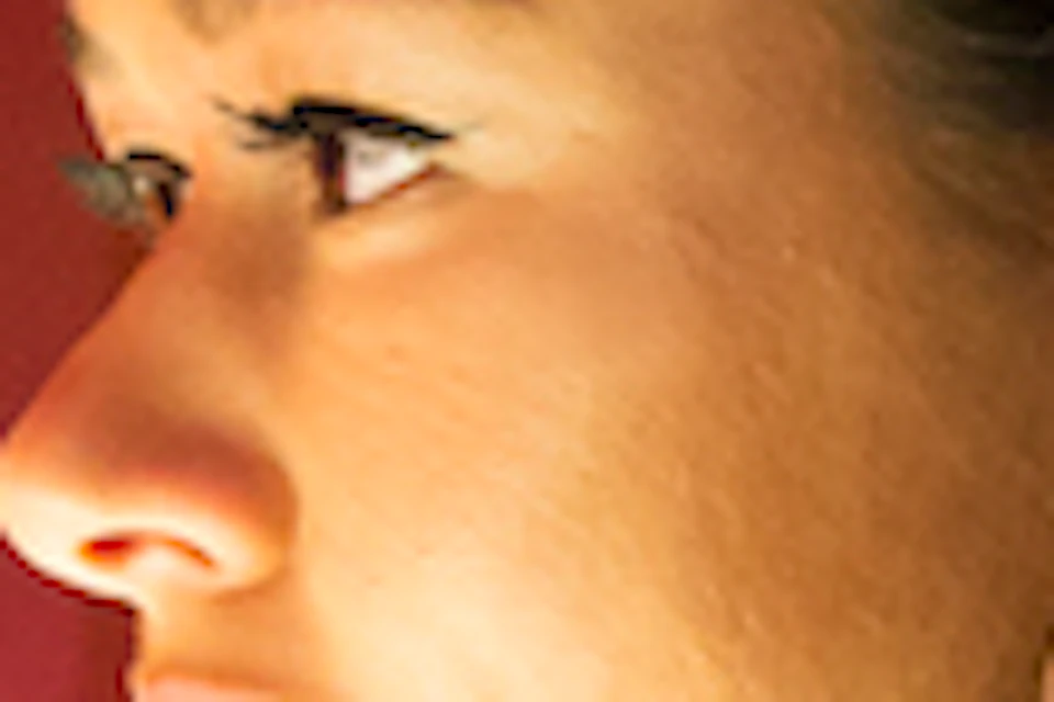 A woman with hoop earrings smells from a glass vial in a vibrant, multi-colored room with numbered panels on the wall.