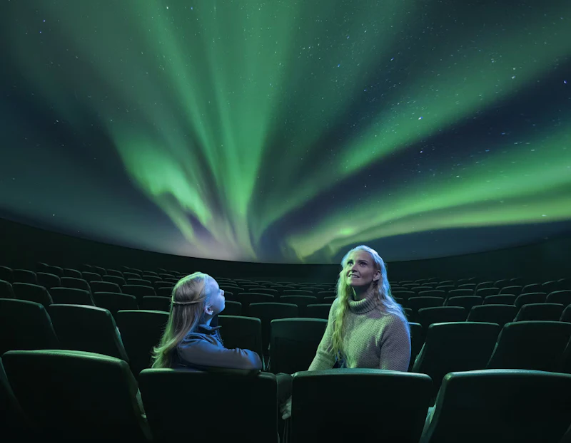 プラネタリウムに座って、ドームにオーロラが映し出されているのを見ている2人の人物。