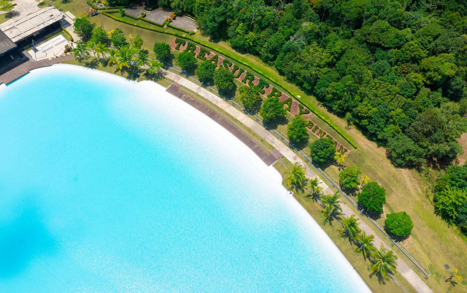 Aerial view of a large turquoise pool surrounded by greenery with the words 'Treasure Bay' landscaped on the grass.