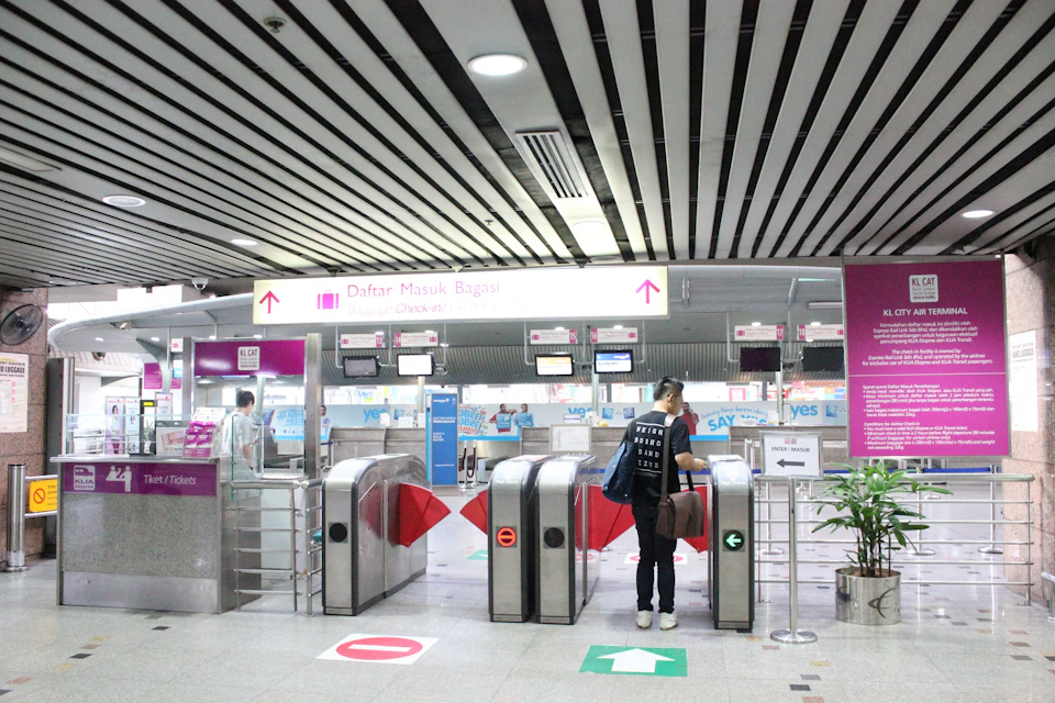 A person passing through a ticket gate at an airport or train station, with check-in counters visible in the background.