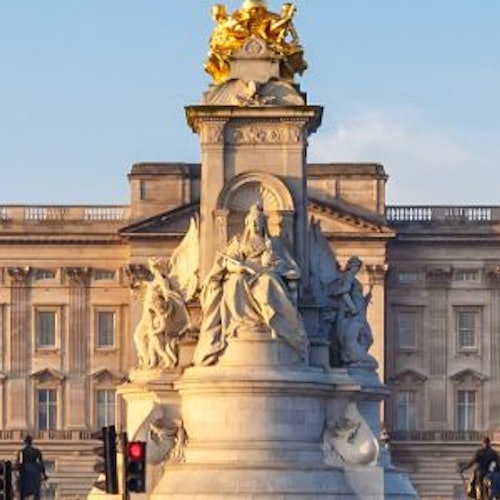 Buckingham Palace - Ein großes Gebäude mit einer großen Statue davor, umgeben von Straßenlaternen und Bäumen, unter einem klaren blauen Himmel. Buckingham Palace - Ein großes Gebäude mit einer großen Statue davor, umgeben von Straßenlaternen und Bäumen, unter einem klaren blauen Himmel.