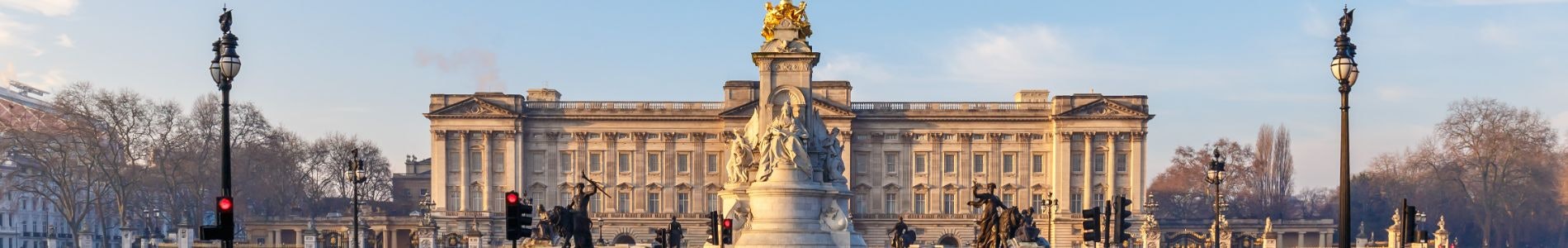 Un grand bâtiment avec une grande statue devant, entouré de lampadaires et d'arbres, sous un ciel bleu clair.