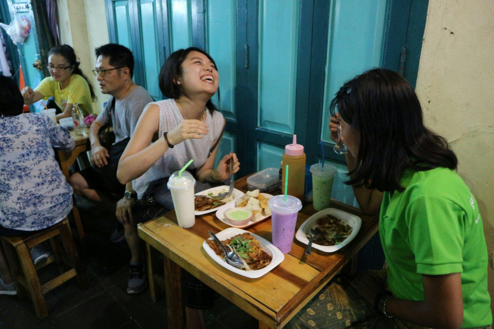 A group of people enjoying a meal at a small restaurant with wooden tables and colorful beverages on the table.