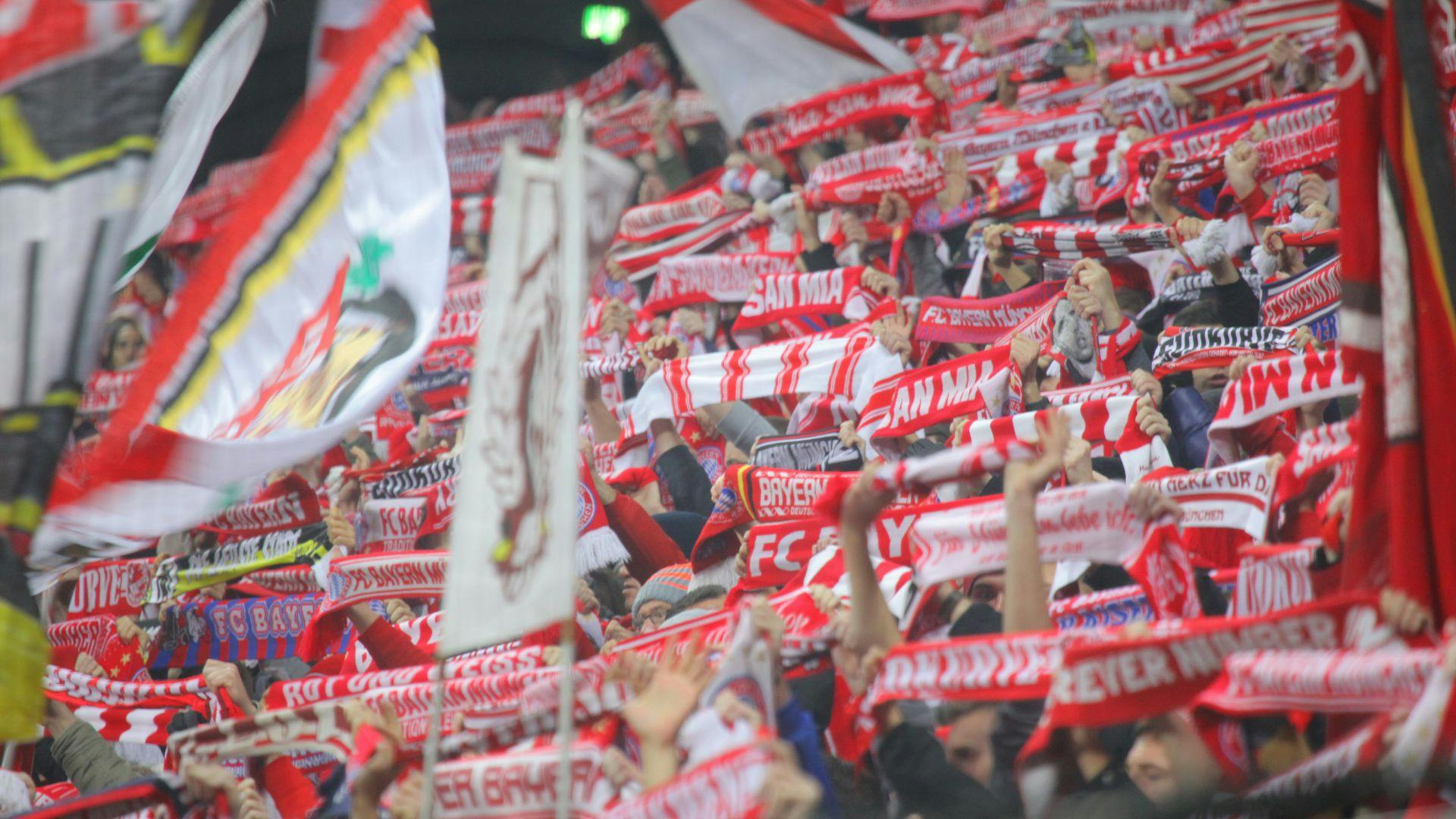 Velký dav sportovních fanoušků, kteří drží červené a bílé šátky s týmovými logy a textem na stadionu a ukazují vzrušení.